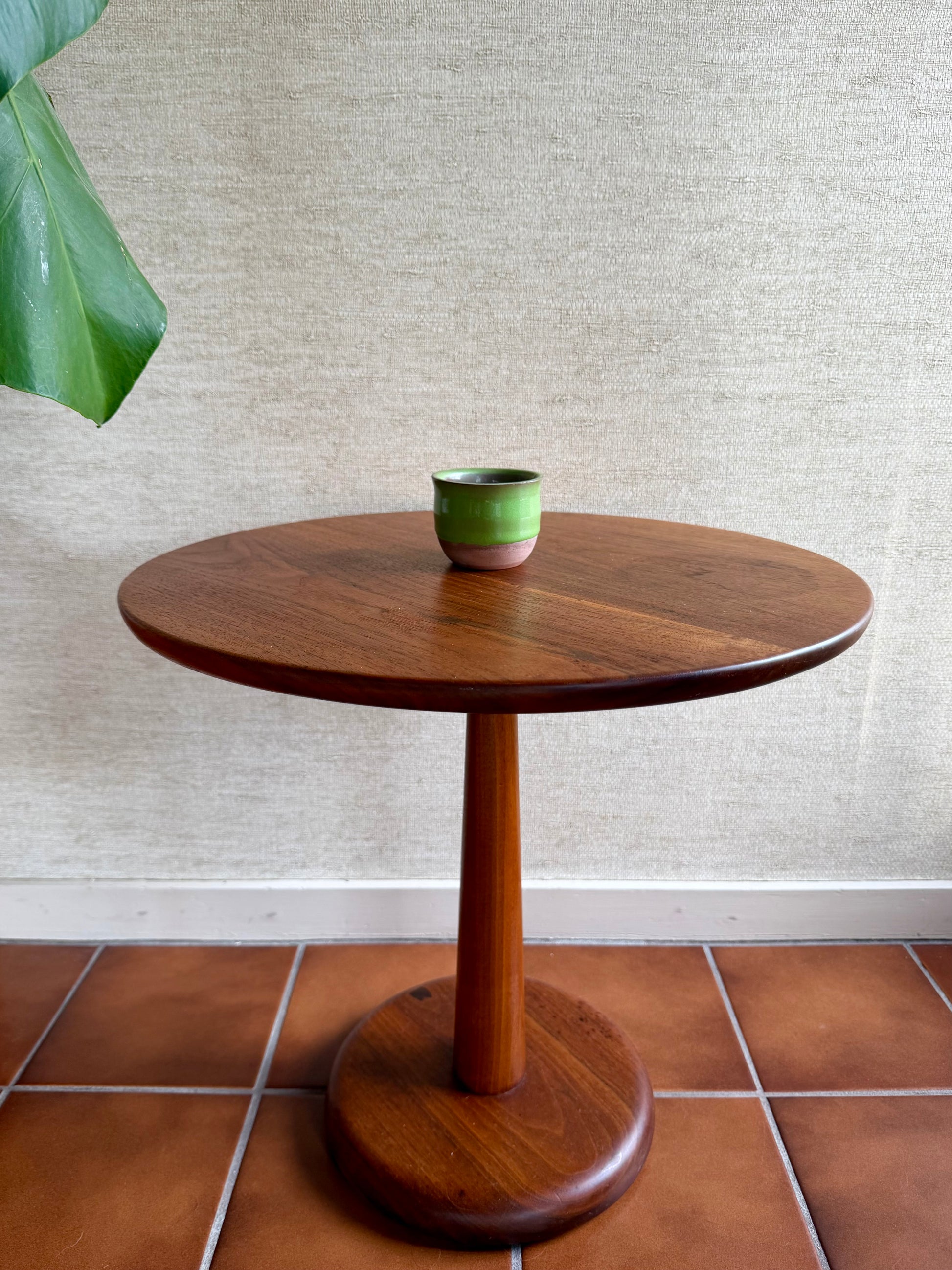 Wooden side table with a green ceramic cup on a textured wall and tiled floor background