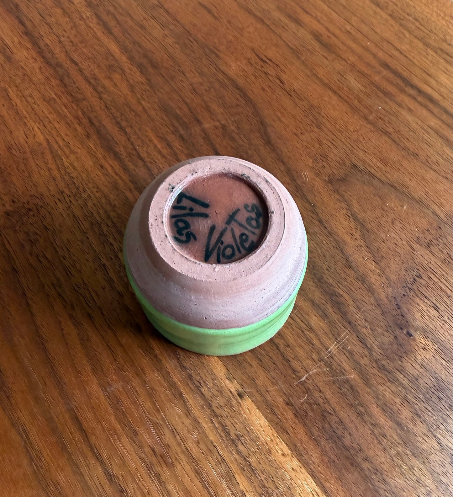 Small ceramic container with a green base and pink top on a wooden surface