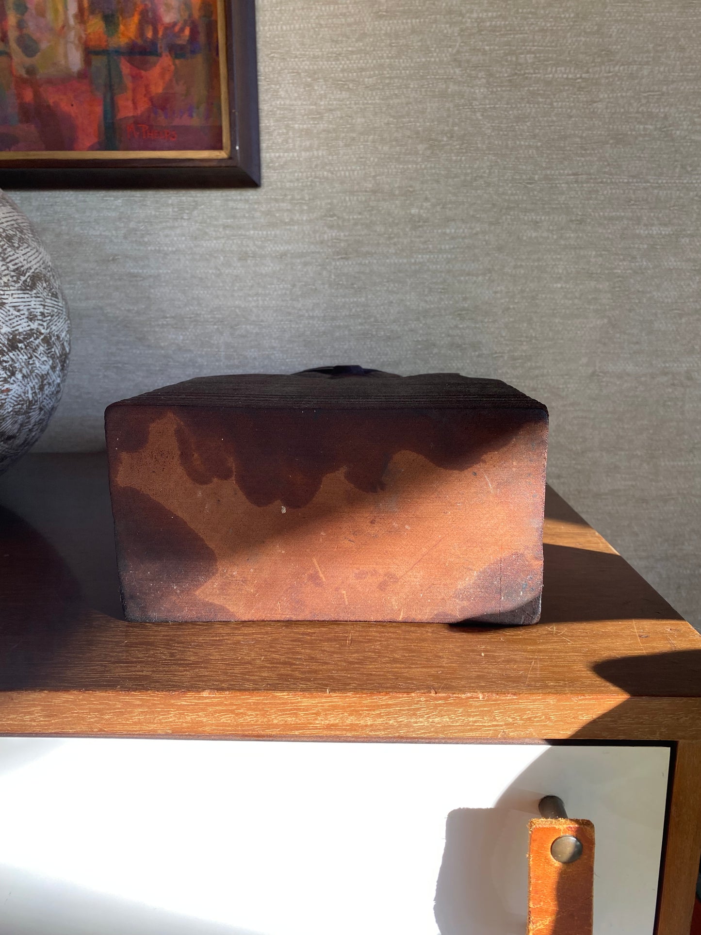 Wooden block with a textured surface leaning against a wall.