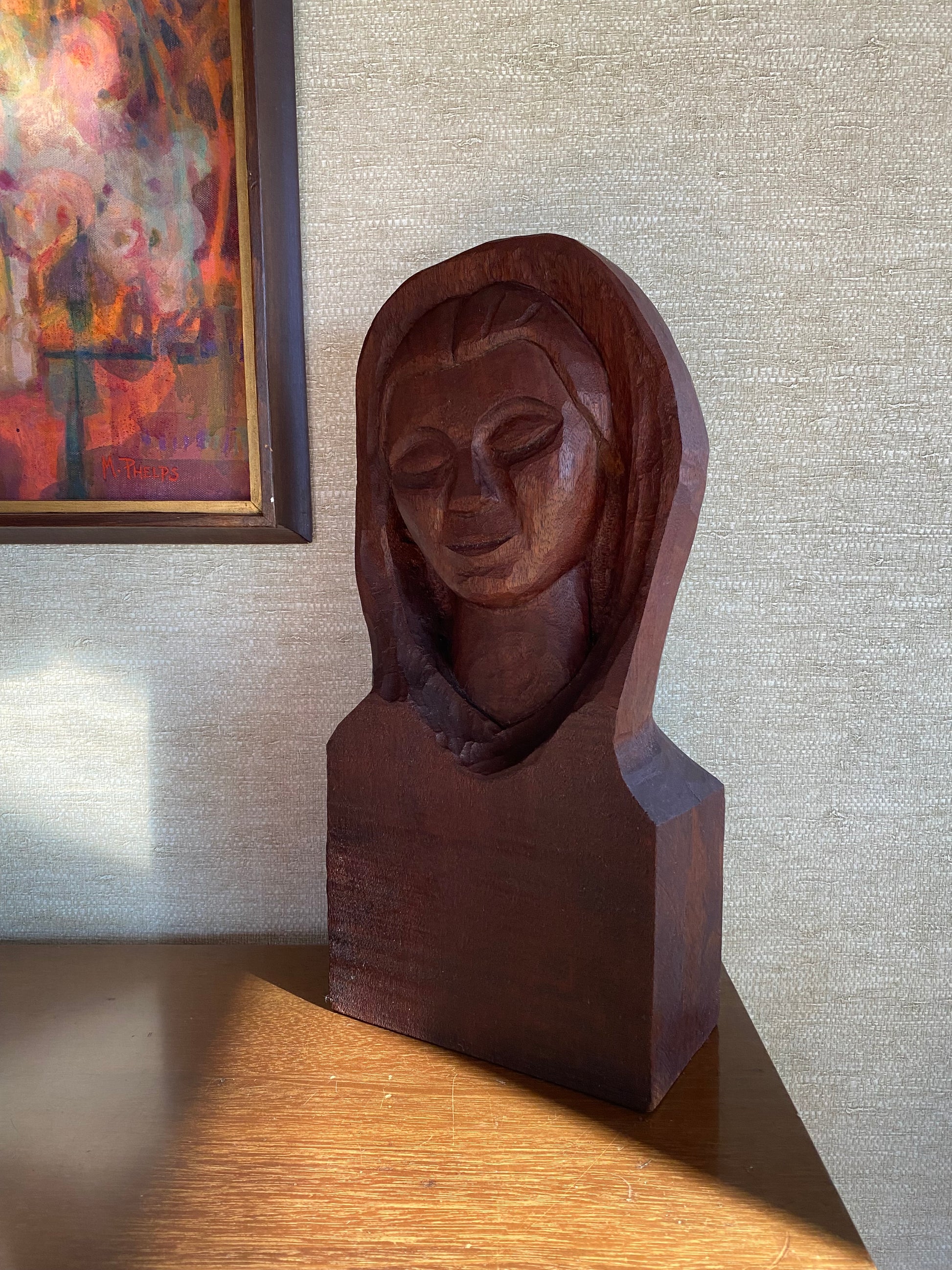 Wooden carvings of faces on a textured wall with a painting in the corner.