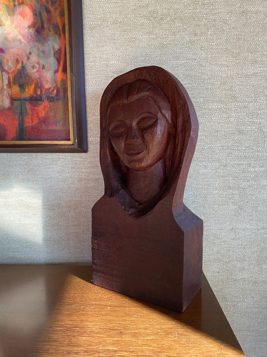 Wooden carvings of faces on a textured wall with a painting in the corner.