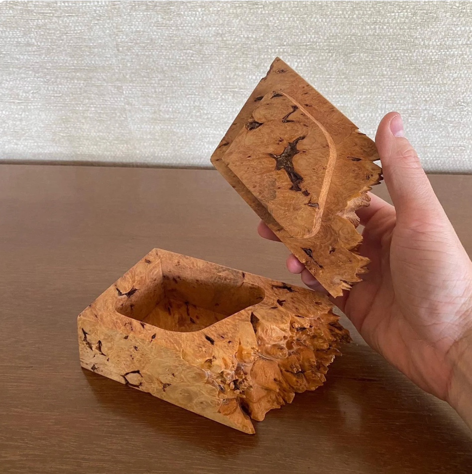 Hand holding a wooden box with a textured surface on a wooden table.