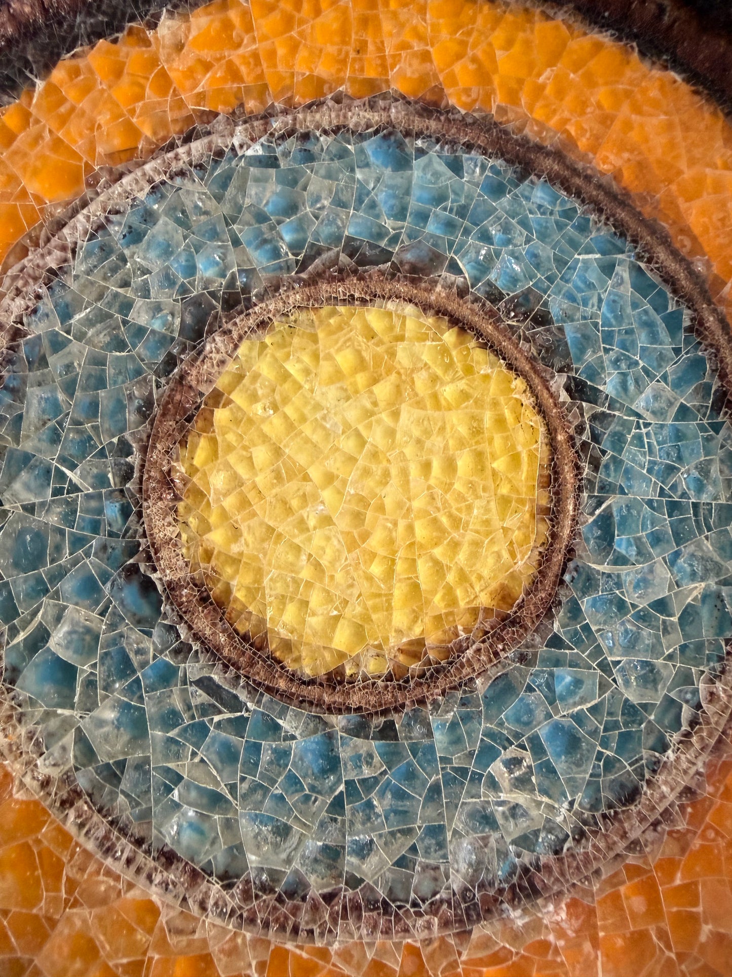 Mosaic design with concentric circles of blue, yellow, and brown on a textured background