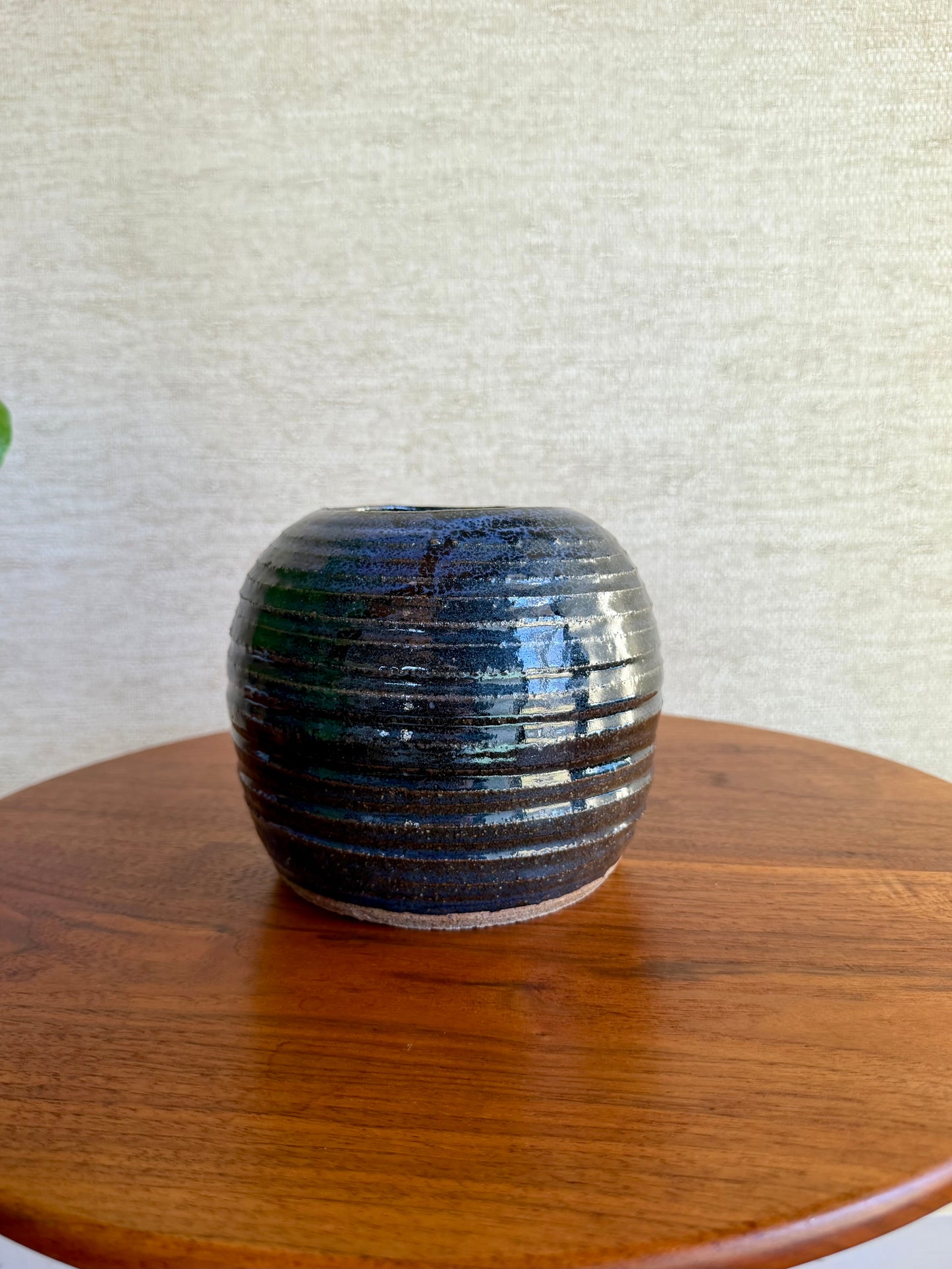 Ceramic vase with ribbed texture on a wooden surface against a textured white wall