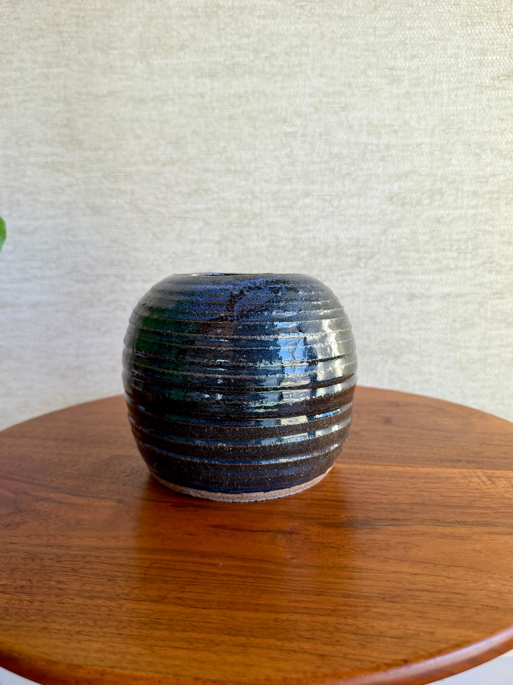Ceramic vase with ribbed texture on a wooden surface against a textured white wall