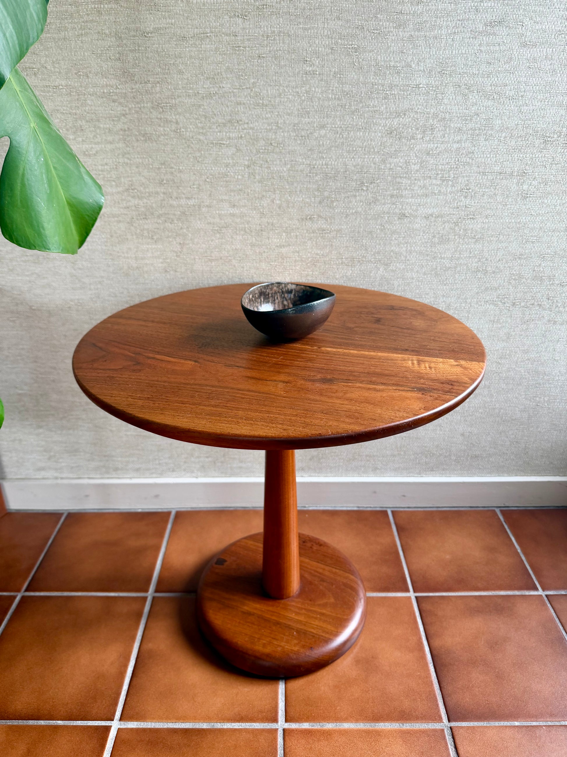 Wooden side table with a bowl on a tiled floor against a textured wall.