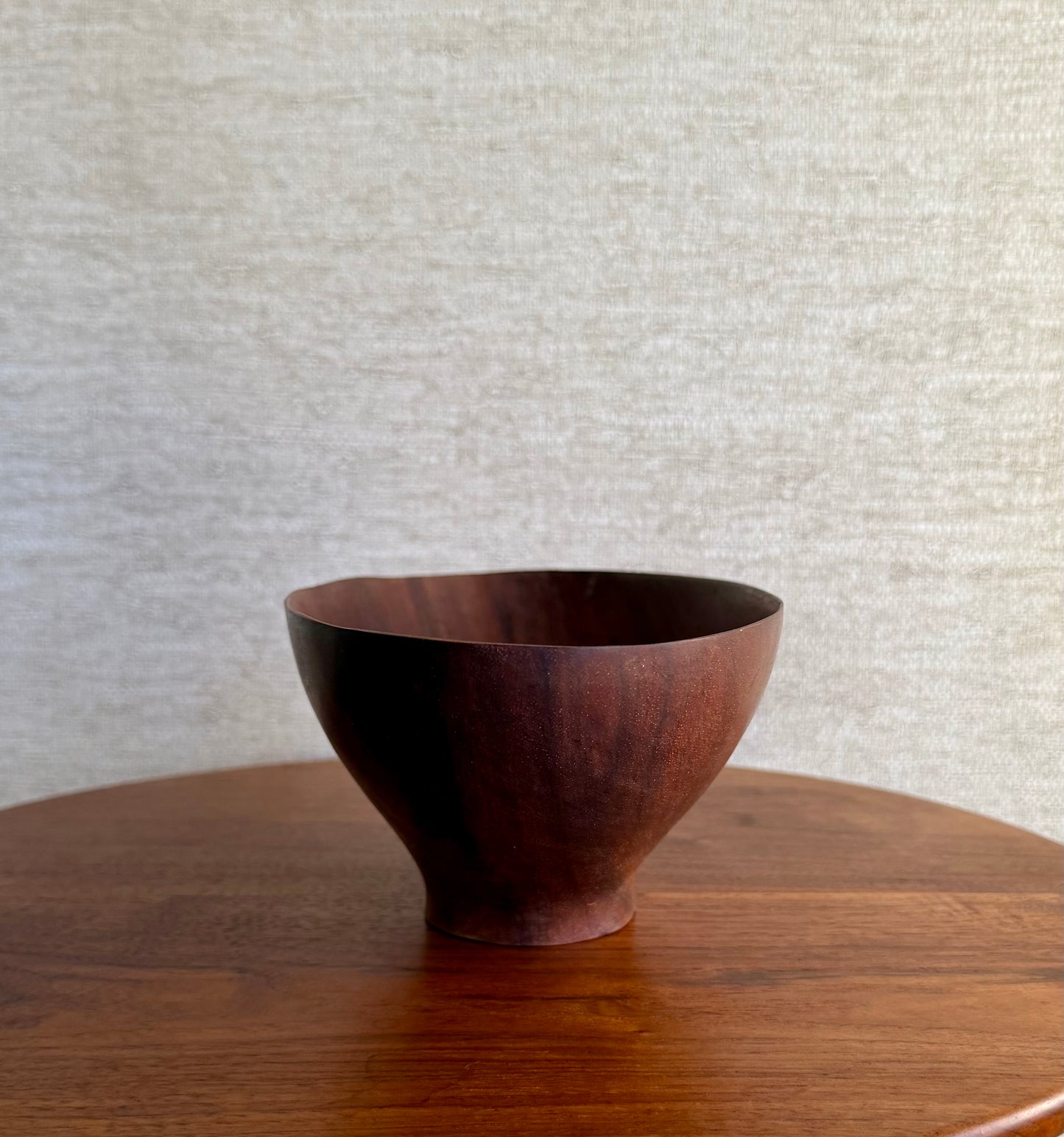Wooden bowl on a wooden surface with a textured light gray wall in the background