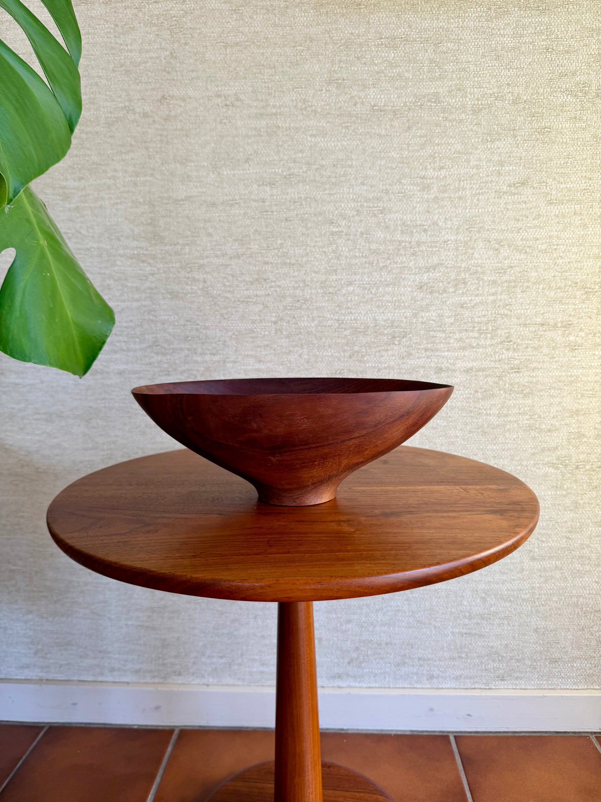 Wooden bowl on a round wooden table against a textured wall.