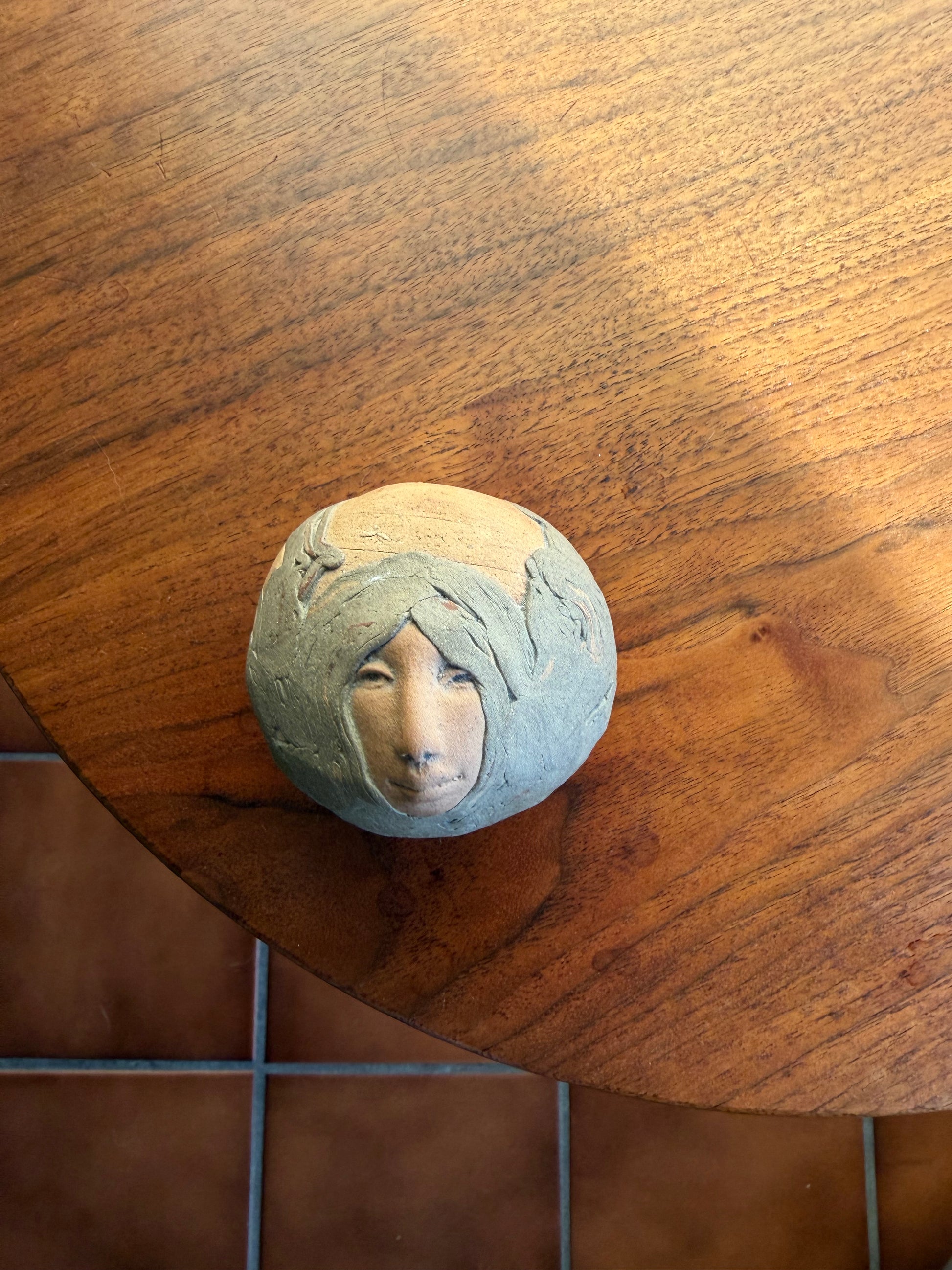 Round Pottery box with a face carved into it on a wooden surface