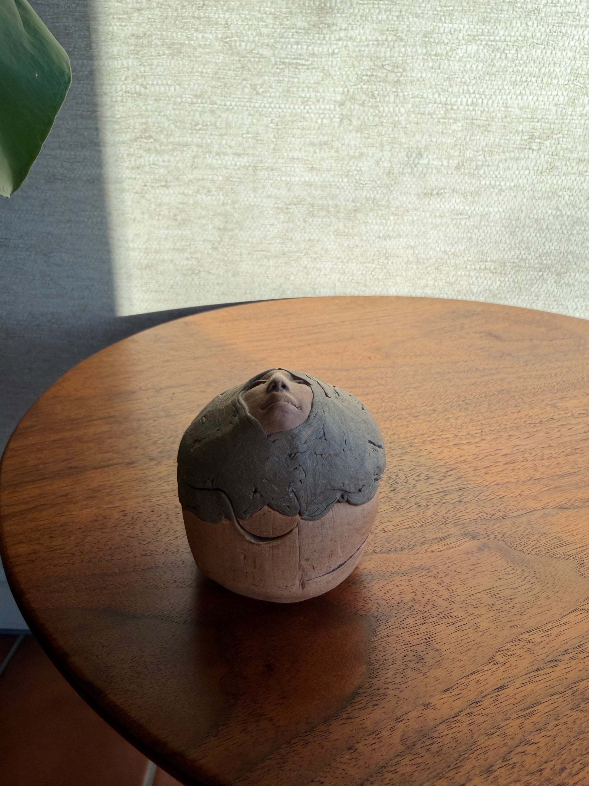 Round Pottery box with a face carved into it on a wooden surface