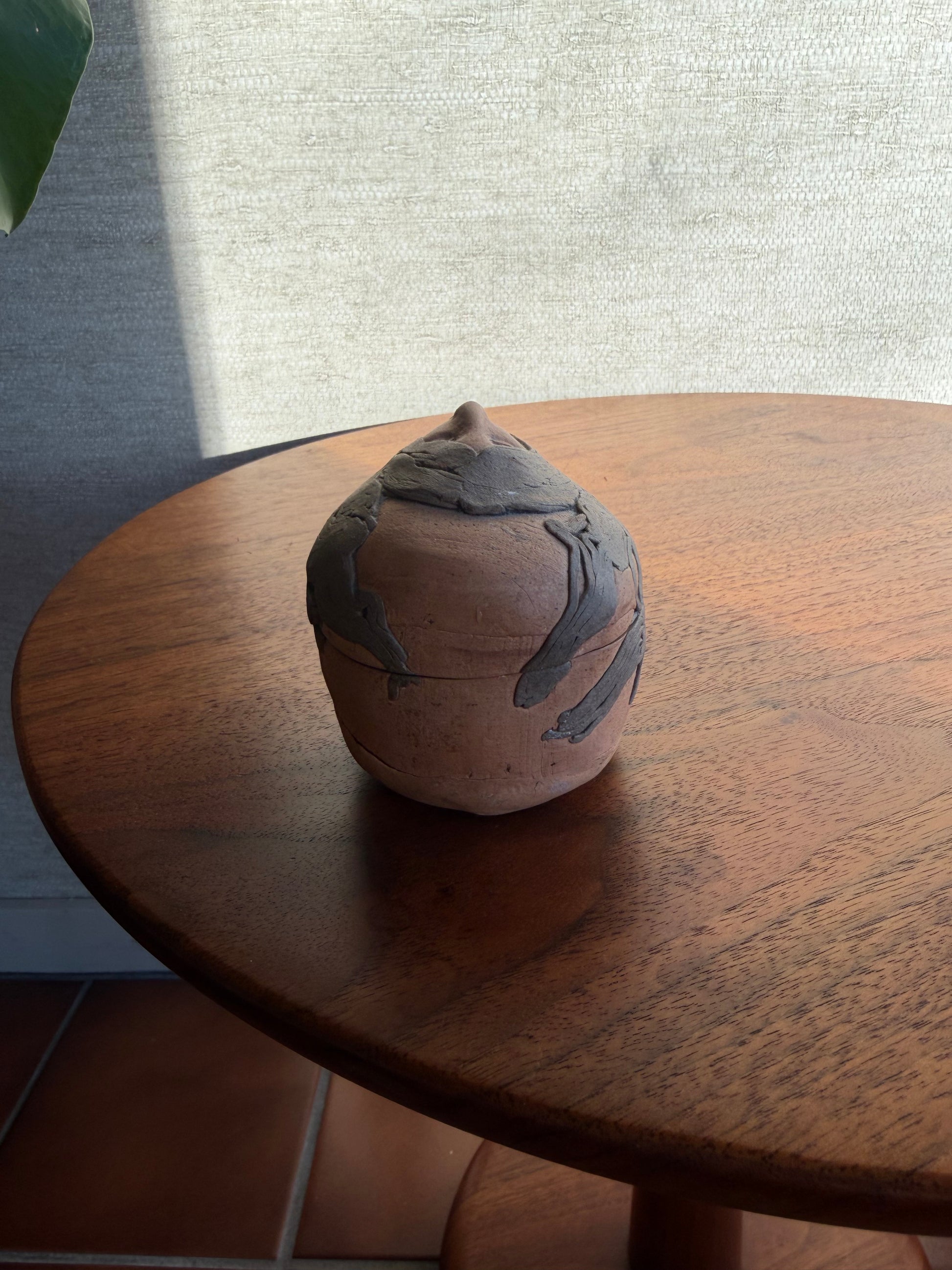 Round Pottery box with a face carved into it on a wooden surface