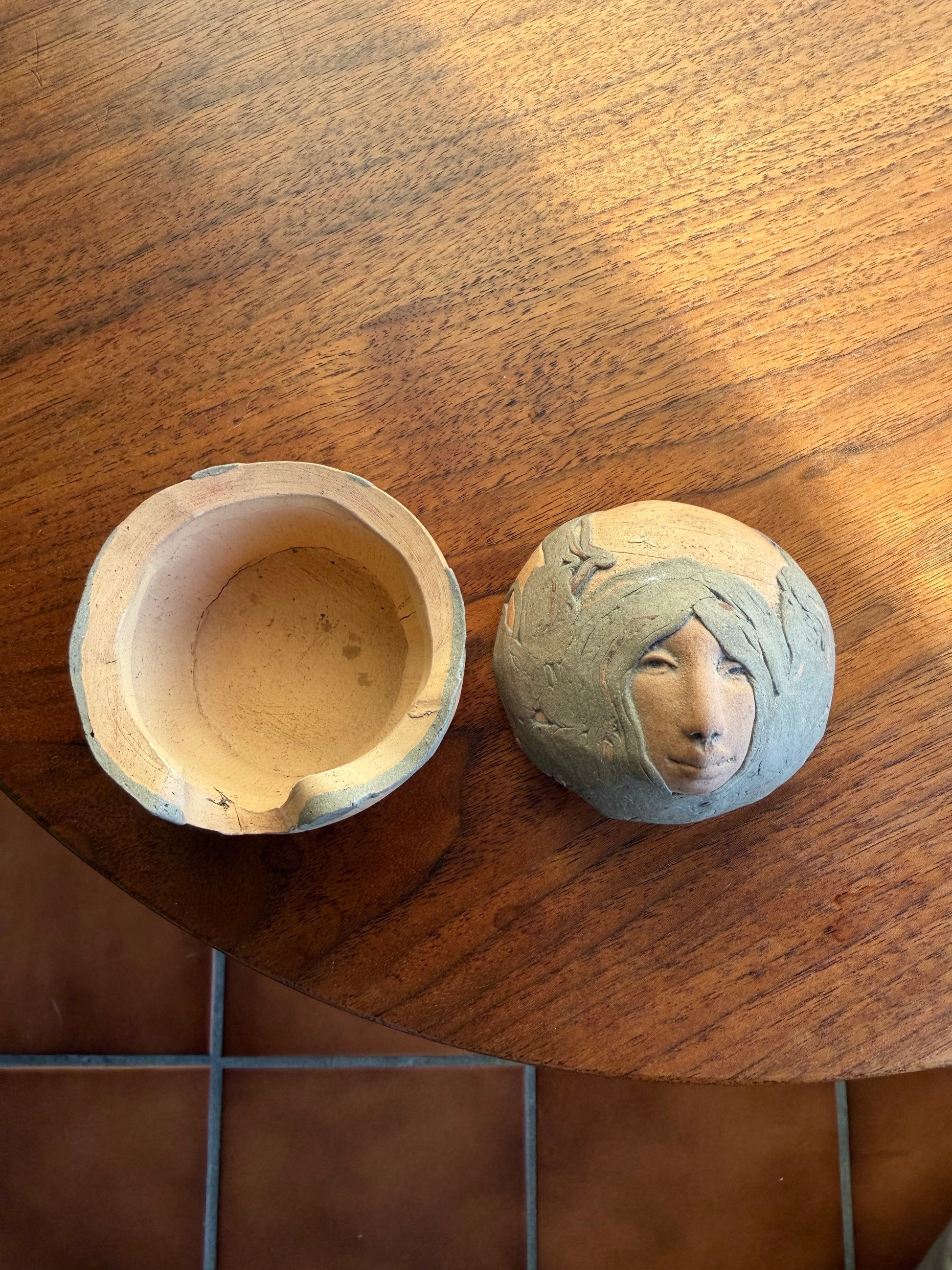 Round Pottery box with a face carved into it on a wooden surface