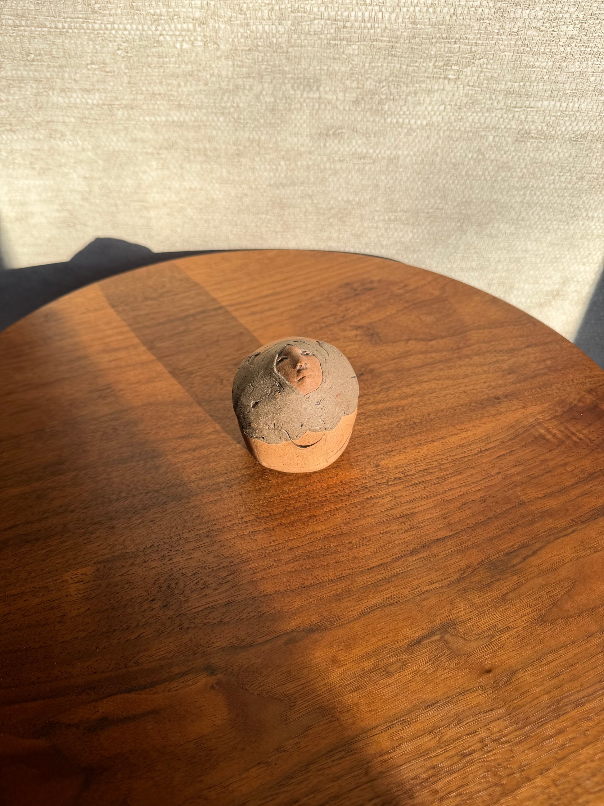 Round Pottery box with a face carved into it on a wooden surface