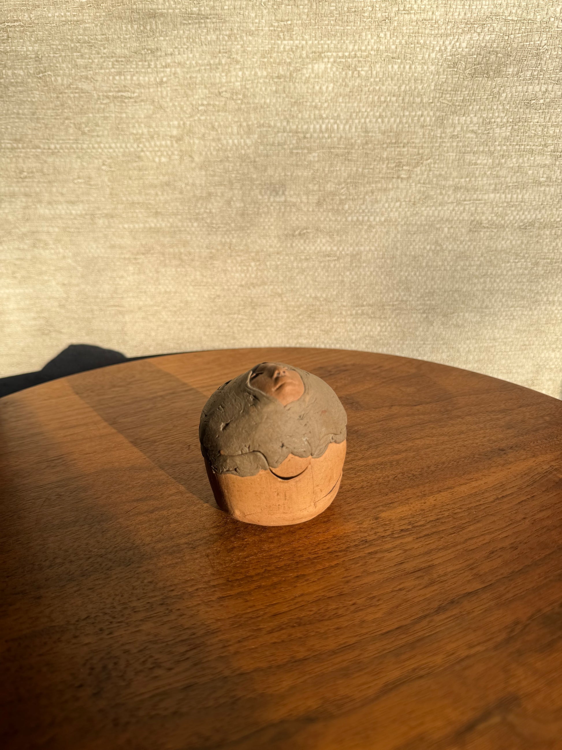 Round Pottery box with a face carved into it on a wooden surface