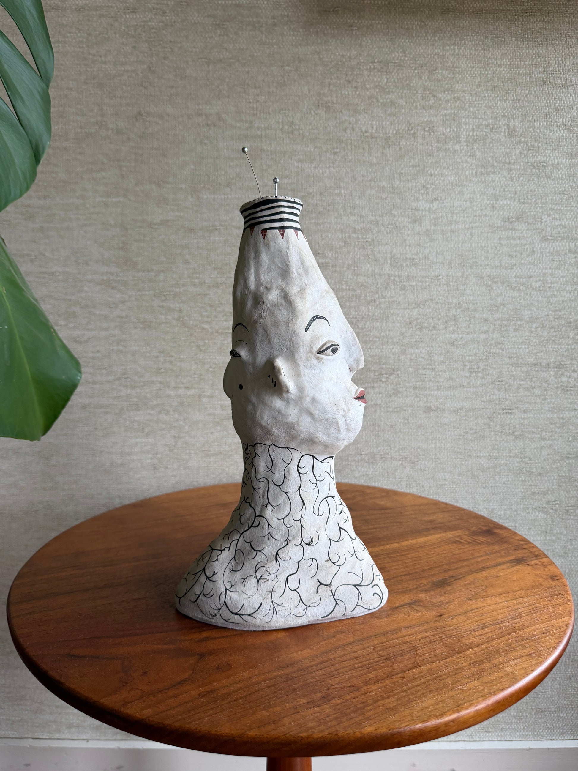 Decorative face vase with a ceramic face on a wooden stand against a neutral wall.