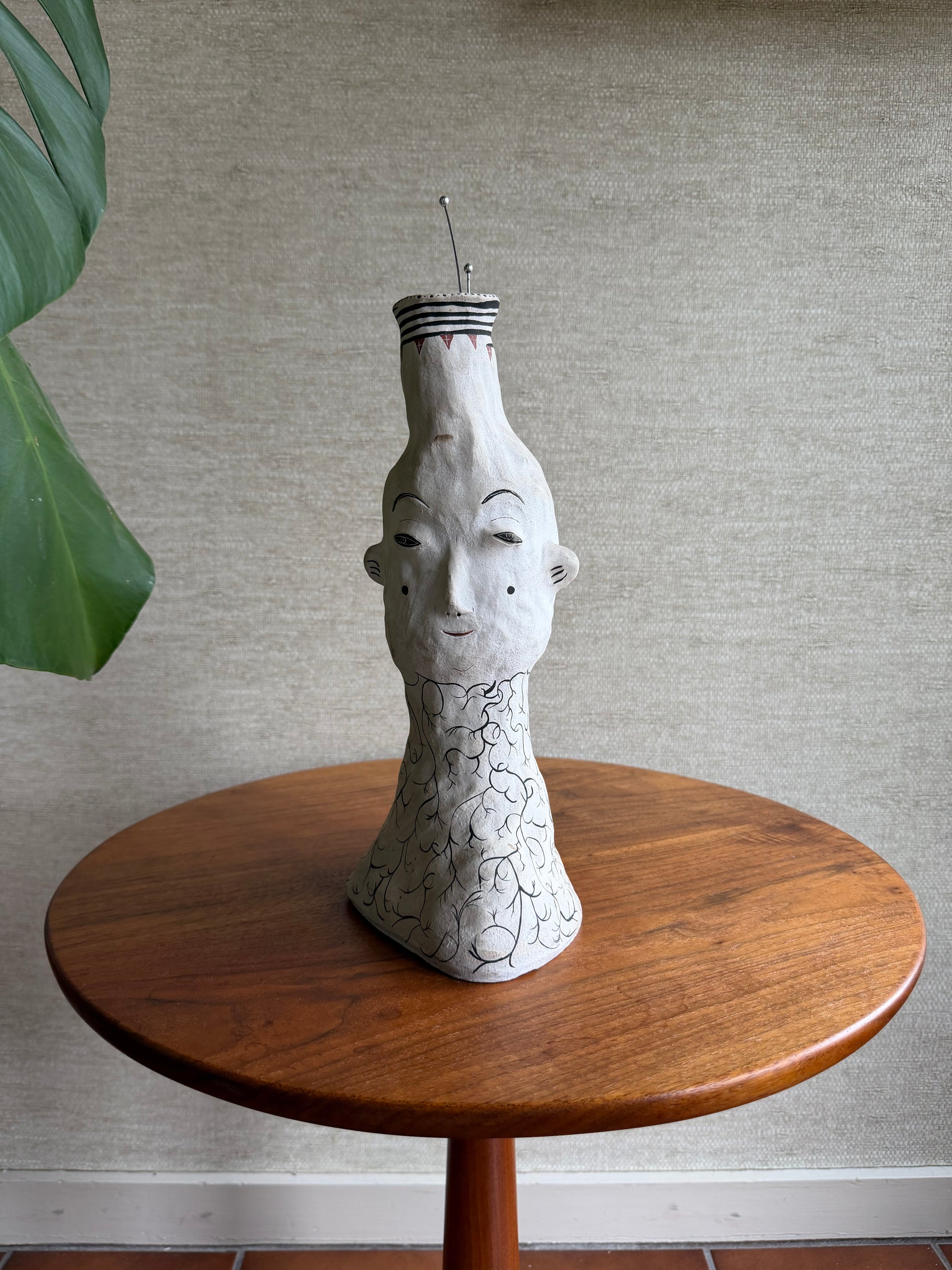 Decorative face vase with a ceramic face on a wooden base against a neutral wall.