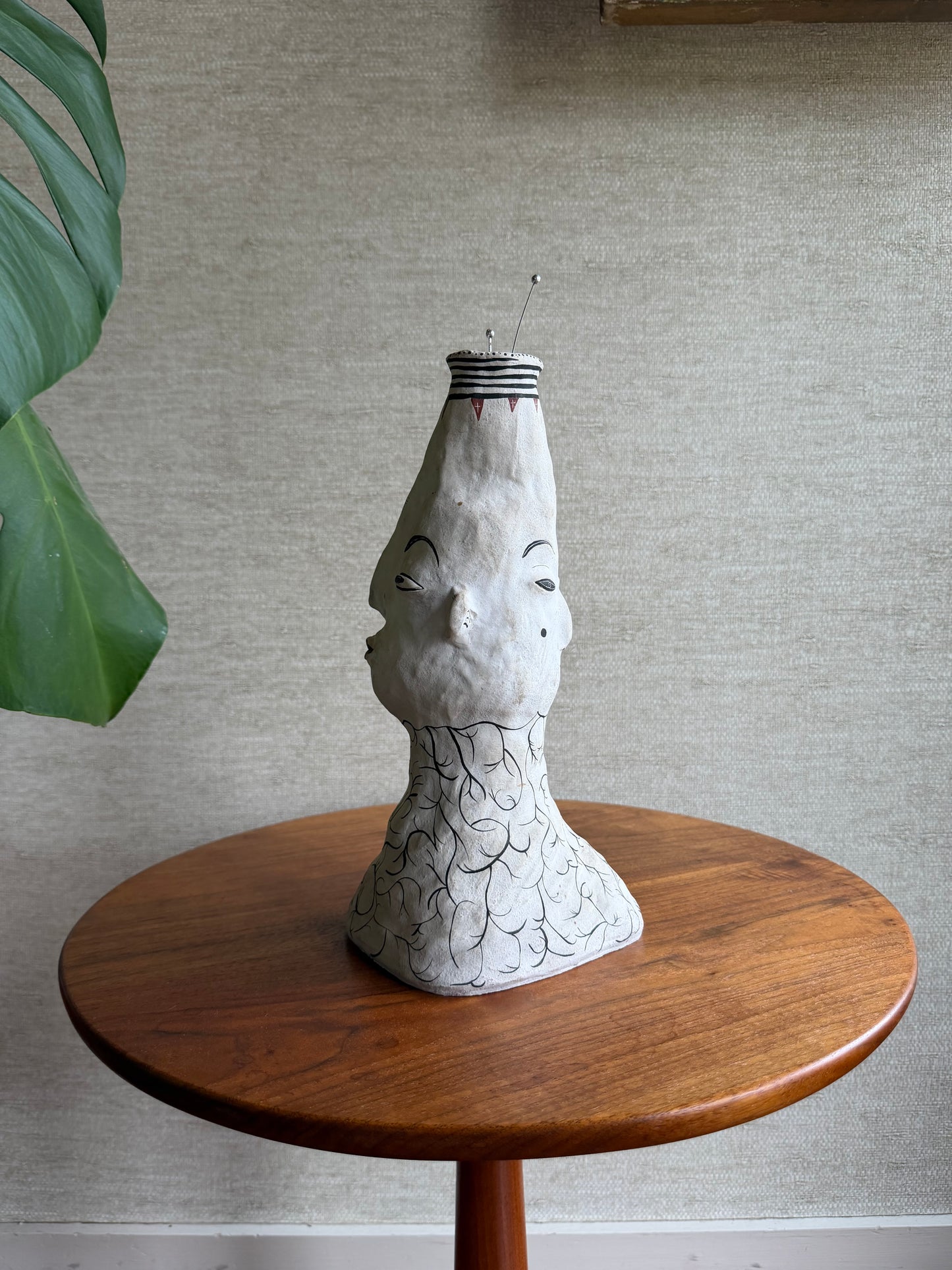 Decorative face vase with a cracked ceramic head on a wooden base against a neutral wall.