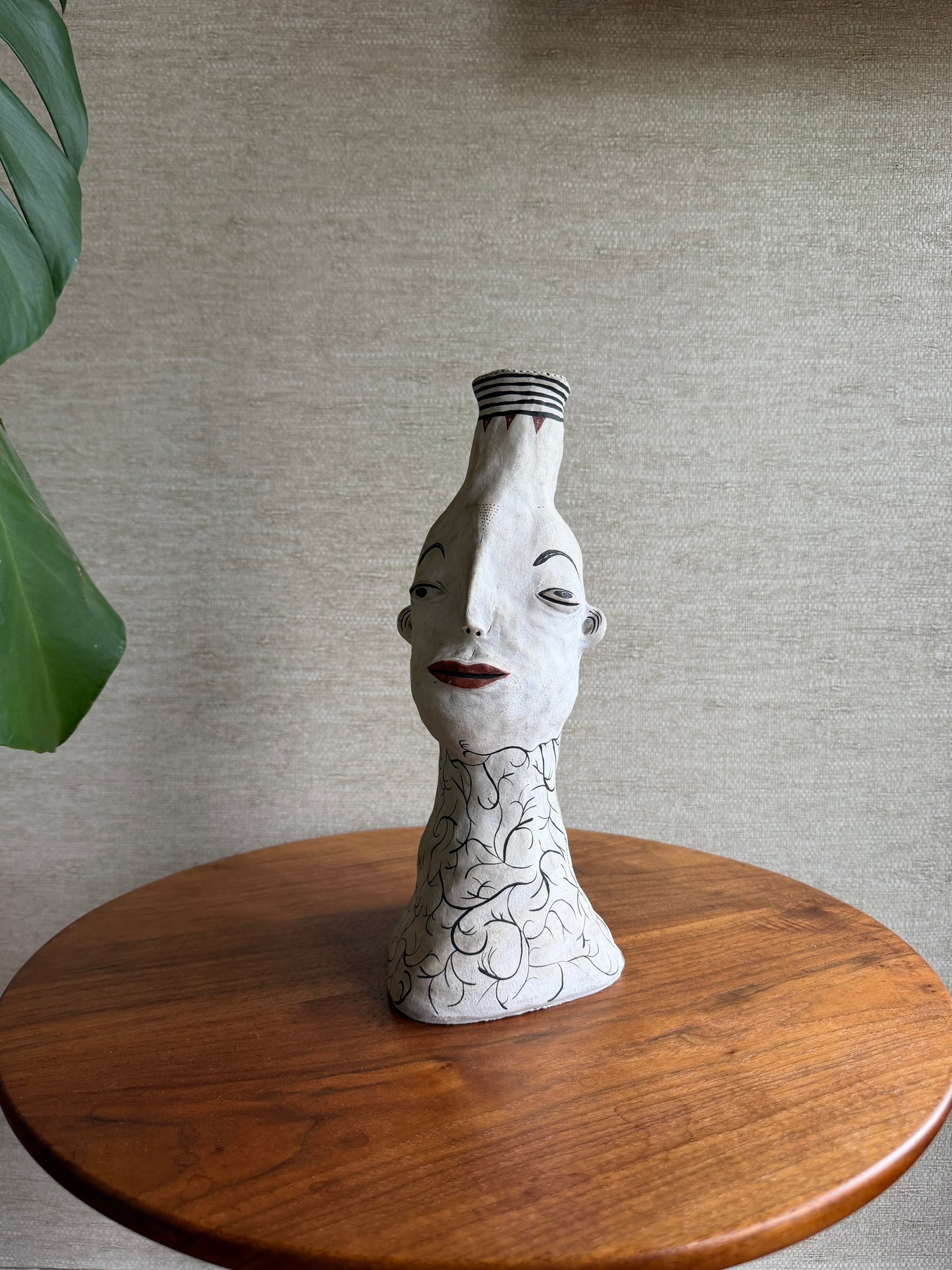 Decorative sculpture of a stylized face on a wooden platform against a neutral wall.