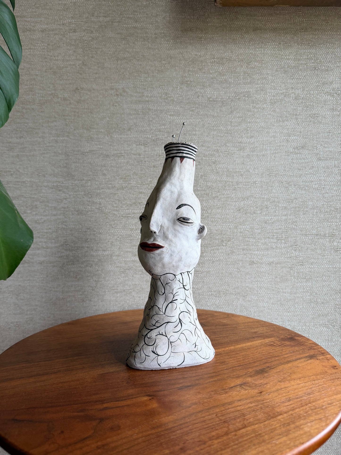 White ceramic head sculpture on a wooden pedestal against a gray wall.